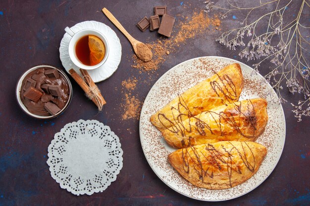 Vista superior deliciosos pastéis assados com xícara de chá no espaço escuro