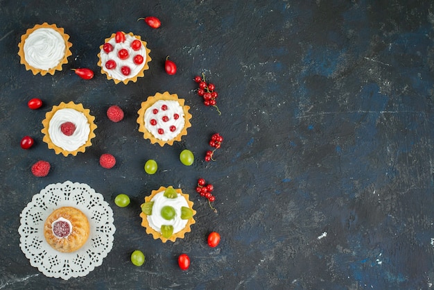 Vista superior distante bolinhos deliciosos com creme e frutas frescas na mesa de frutas escura