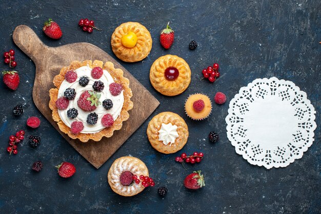 Vista superior distante, um bolo gostoso com creme e frutas vermelhas junto com biscoitos de pulseira em um biscoito de bolo de frutas silvestres escuro