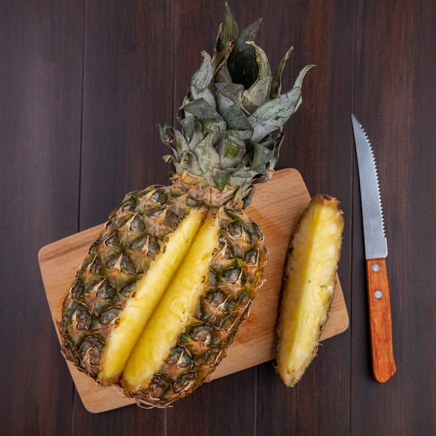 Vista superior do abacaxi com um pedaço cortado de frutas inteiras na tábua com faca na superfície de madeira