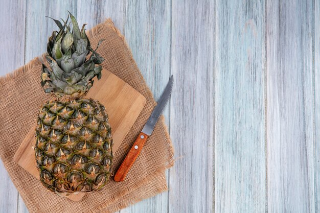 Vista superior do abacaxi na tábua com faca no pano de saco e superfície de madeira