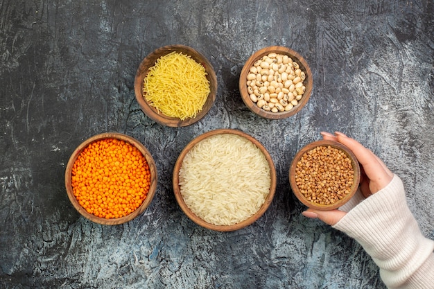 Foto grátis vista superior do arroz cru com vermicelli e trigo sarraceno cru dentro de pequenos potes na mesa cinza claro