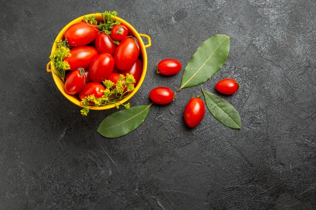 Vista superior do balde amarelo de tomate cereja e folhas de louro com flores de endro e tomate cereja no chão escuro com espaço de cópia