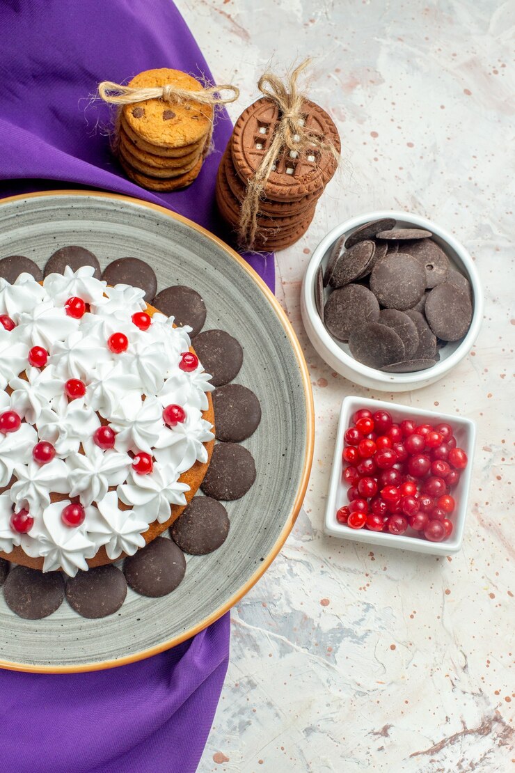 Foto grátis vista superior do bolo com creme de confeiteiro no prato, biscoitos xale roxos amarrados com corda de chocolate e frutas em tigelas na mesa branca