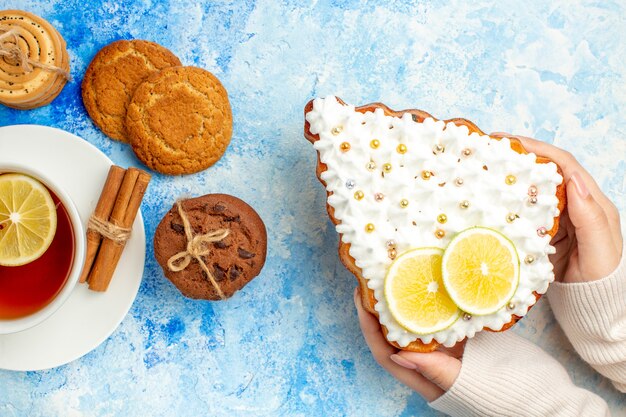 Vista superior do bolo da árvore de natal em uma xícara de chá de biscoitos de mão feminina na mesa azul