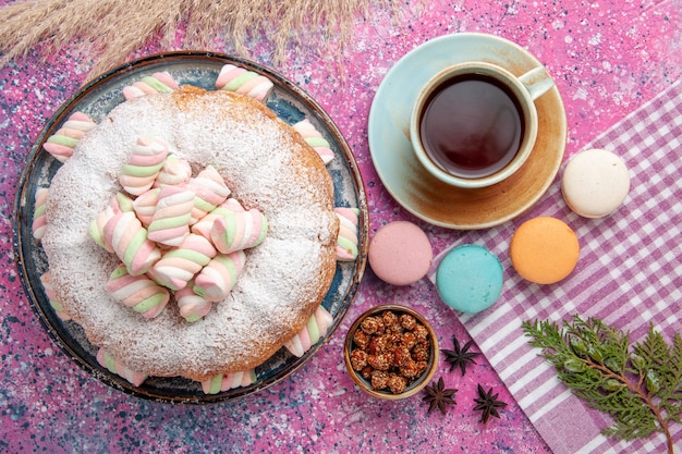 Vista superior do bolo de confeiteiro com marshmallows e uma xícara de chá na superfície rosa