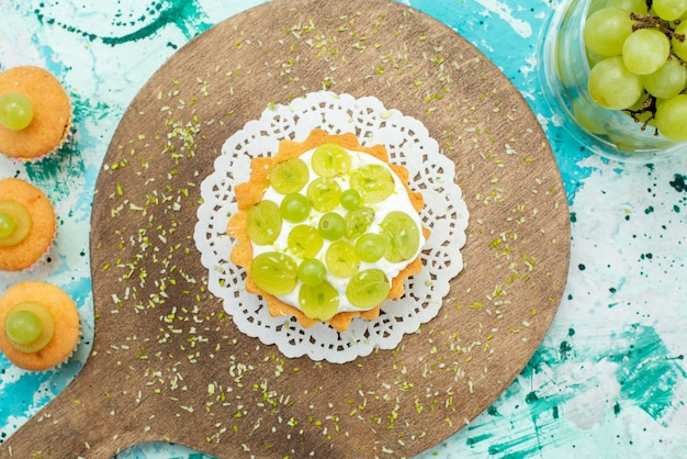 Foto grátis vista superior do bolo gostoso com creme delicioso e biscoitos de uvas frescas e fatiados na foto doce do bolo de mesa com luz azul