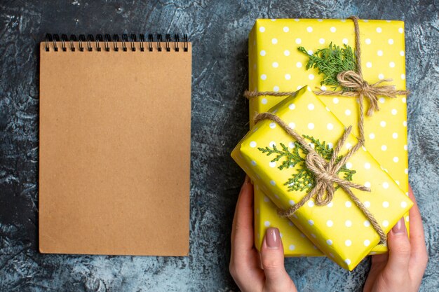 Vista superior do caderno e a mão segurando uma das caixas de presente de Natal amarela em fundo escuro