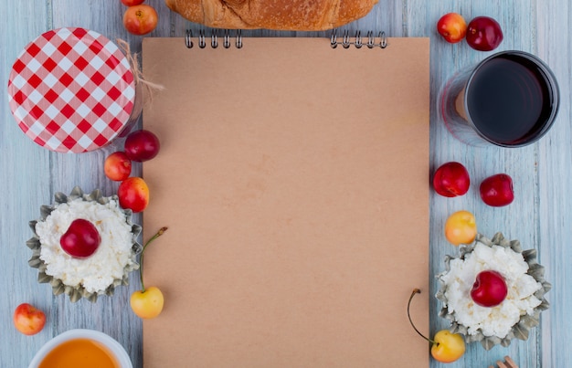 Foto grátis vista superior do caderno e queijo cottage com copo de cerejas frescas de amarelas e vermelhas maduras de suco dispostos em torno no fundo cinza