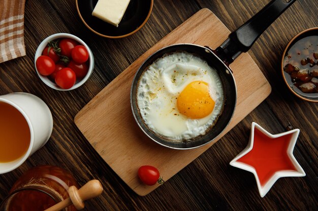 Vista superior do café da manhã com ovo frito na frigideira na tábua com suco de laranja de geléia de manteiga de tomate em fundo de madeira