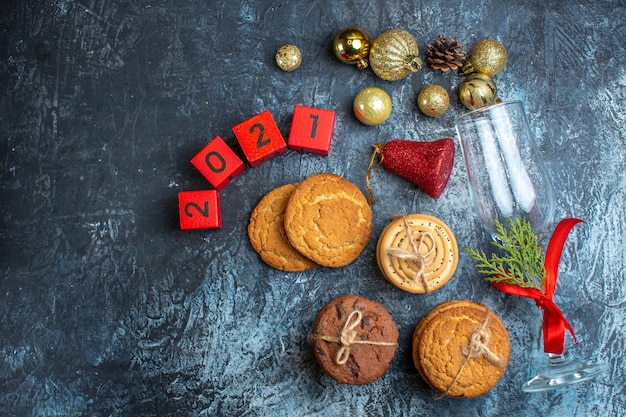 Foto grátis vista superior do cálice de vidro caído com fita vermelha e acessórios de decoração ao lado de números de biscoitos empilhados em fundo escuro