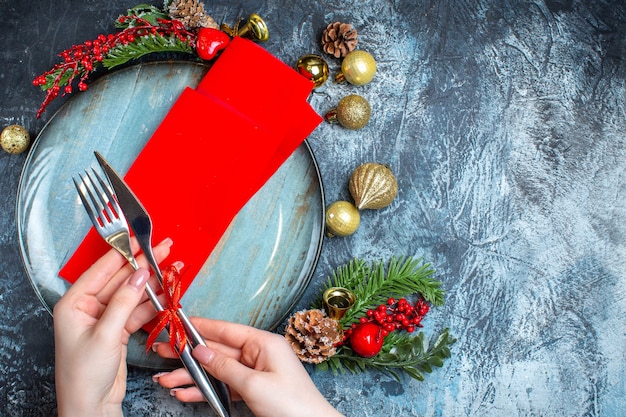 Foto grátis vista superior do clima de natal com a mão definindo um layout de mesa com talheres e prato azul em fundo escuro