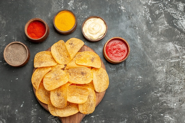 Vista superior do conjunto de batatas fritas contendo diferentes especiarias, maionese e ketchup na mesa cinza