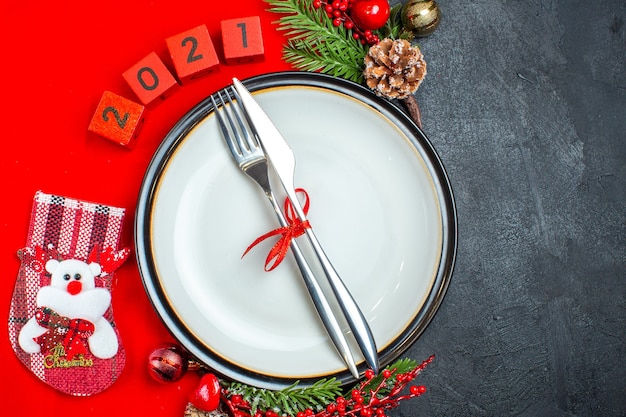 Vista superior do conjunto de talheres no prato de jantar acessórios de decoração ramos de abeto e números meia de natal em um guardanapo vermelho sobre um fundo preto