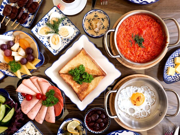 Vista superior do conjunto de vários pratos de comida no café da manhã ovos fritos com tomate salada de frutas presunto legumes torradas de queijo