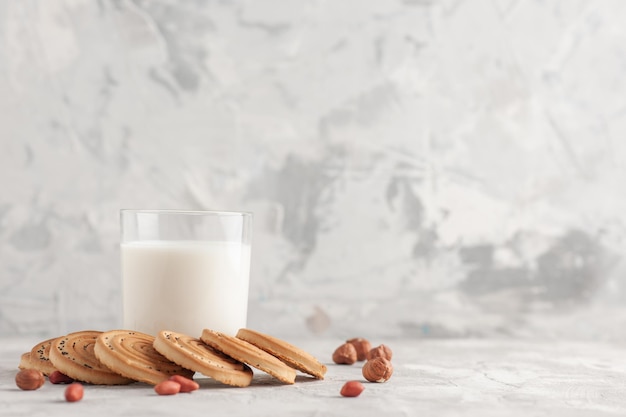Vista superior do copo de vidro cheio de leite e biscoitos amendoins no lado direito no fundo branco manchado com espaço livre