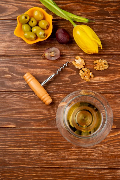 Foto grátis vista superior do copo de vinho branco com saca-rolhas de noz de azeitona e flores na mesa de madeira