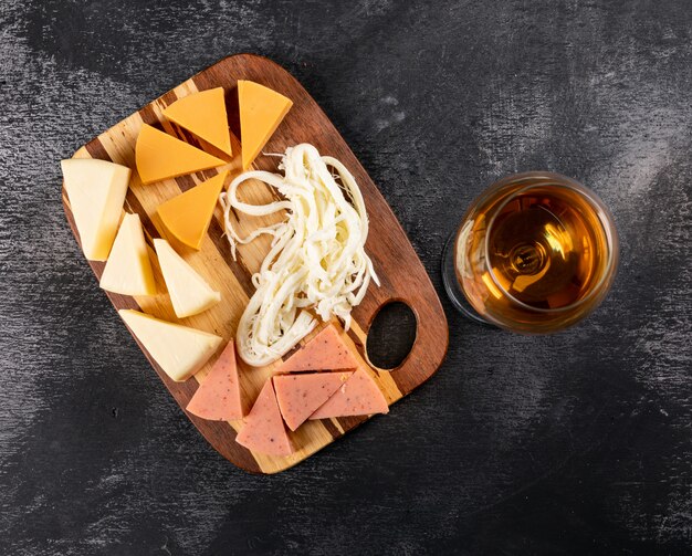 Vista superior do copo de vinho e queijo na tábua de madeira no escuro horizontal