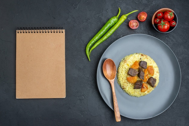 Vista superior do delicioso arroz pilaf cozido com fatias de carne e tomate na superfície escura