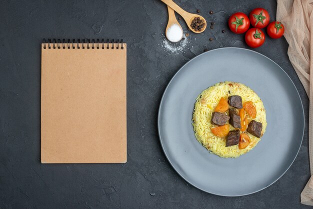 Vista superior do delicioso arroz pilaf cozido com fatias de carne e tomate na superfície escura