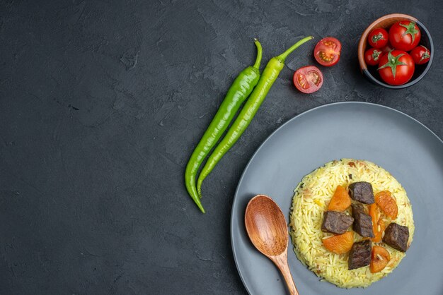 Vista superior do delicioso arroz pilaf cozido com fatias de carne e tomate na superfície escura