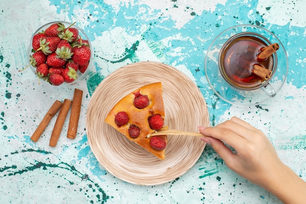 Vista superior do delicioso bolo de morango fatiado em fatias de bolo saboroso com chá de canela e morangos vermelhos frescos em uma mesa azul brilhante, bolo para assar massa doce