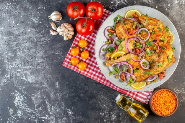 Vista superior do delicioso jantar prato de frango frito com várias especiarias e alimentos tomates com caules de lentilha vermelha alhos caídos garrafa de óleo limão no lado esquerdo no fundo de cor escura