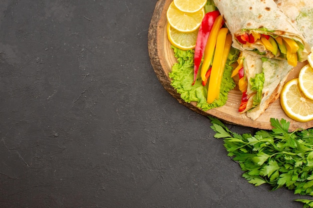 Foto grátis vista superior do delicioso sanduíche de frango fatiado shaurma com limão e verduras no escuro