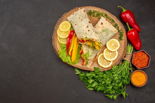 Vista superior do delicioso sanduíche de frango fatiado shaurma com limão e verduras no escuro