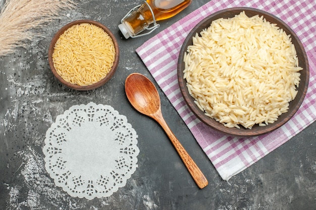 Vista superior do frasco de óleo caído de toalha de íon de arroz branco cozido e cru e despojado roxo e colher guardanapo