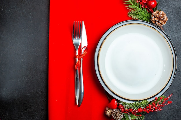 Vista superior do fundo de Natal com acessórios de decoração de prato de jantar, ramos de abeto e talheres em um guardanapo vermelho