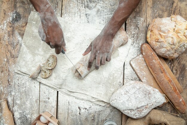 Vista superior do homem afro-americano cozinha cereal fresco, pão, farelo na mesa de madeira. Comer saboroso, nutrição, produto artesanal. Alimentos sem glúten, estilo de vida saudável, fabricação orgânica e segura. Feito à mão.