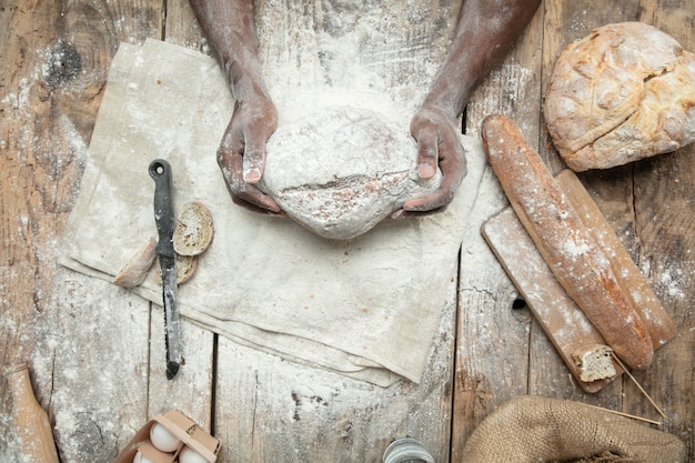 Vista superior do homem afro-americano cozinha cereal fresco, pão, farelo na mesa de madeira. Comer saboroso, nutrição, produto artesanal