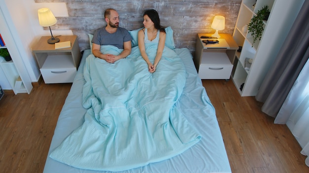 Foto grátis vista superior do jovem casal sob os lençóis da cama pela manhã, tendo uma conversa.