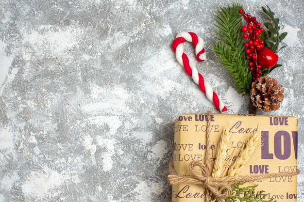 Vista superior do lindo presente de Natal embalado com inscrição de amor e acessórios de decoração de ramos de abeto cone de conífera no lado esquerdo na superfície do gelo