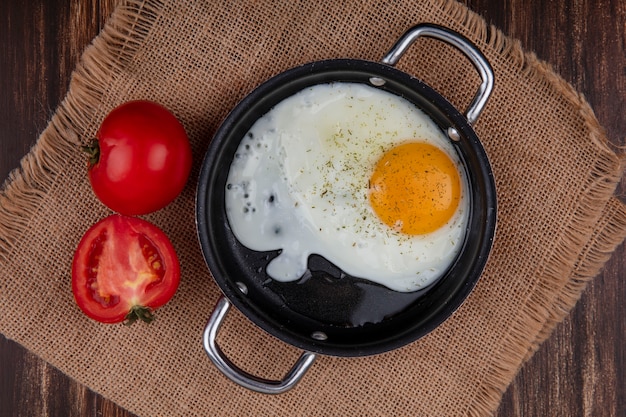 Vista superior do ovo frito em uma panela com tomates em um guardanapo bege em um fundo de madeira