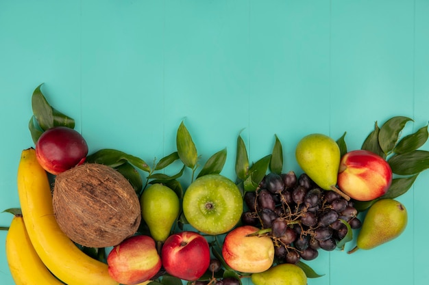 Vista superior do padrão de frutas como coco pera, pêssego, uva, maçã, banana, com folhas em fundo azul com espaço de cópia