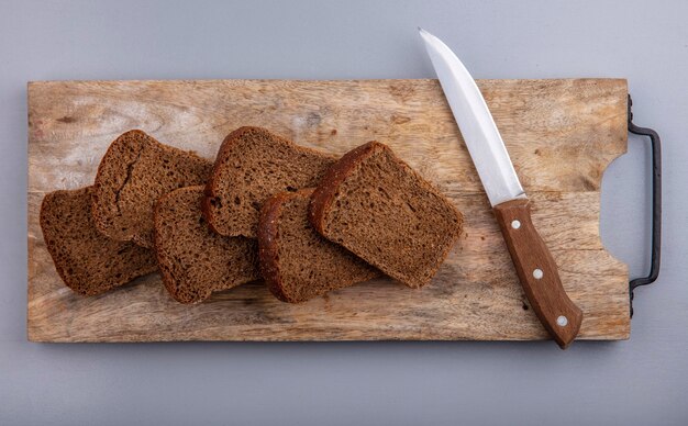 Vista superior do pão de centeio fatiado e faca na tábua em fundo cinza