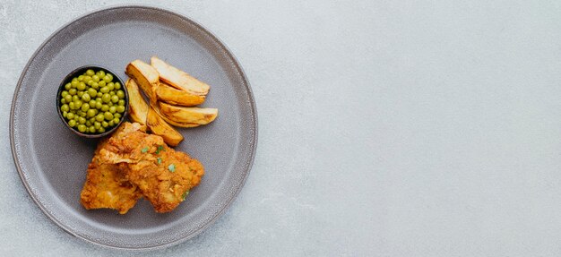 Vista superior do peixe e batatas fritas com ervilhas no prato e copie o espaço