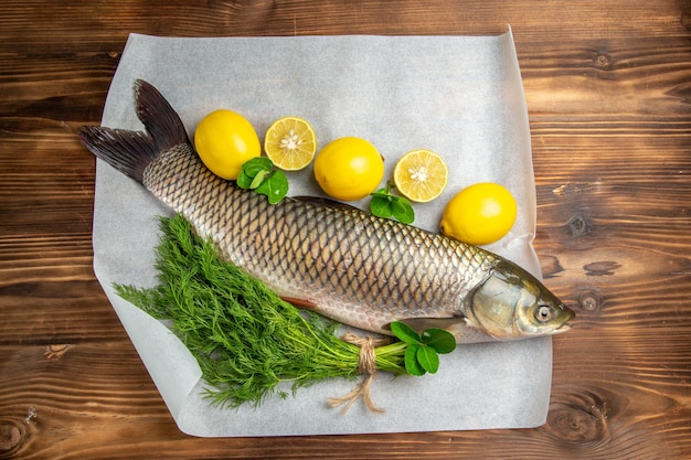 Vista superior do peixe fresco com limão e verduras na mesa marrom