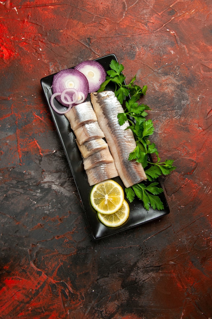 Foto grátis vista superior do peixe fresco fatiado com verduras e pedaços de limão dentro de uma panela preta sobre o fundo escuro
