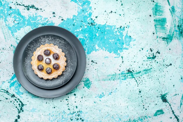 Vista superior do pequeno bolo com açúcar em pó e cerejas dentro do prato em azul claro, torta de bolo de frutas