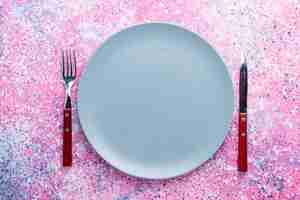 Foto grátis vista superior do prato vazio de cor azul com garfo e faca na parede rosa brilhante prato de foto colorida comida