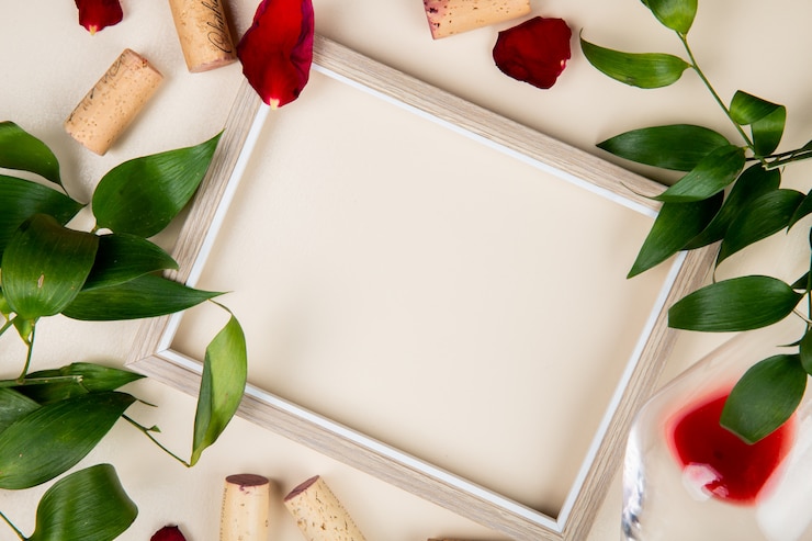 Foto grátis vista superior do quadro com um copo de vinho tinto e rolhas em branco decorado com folhas e pétalas de flores com espaço de cópia 1
