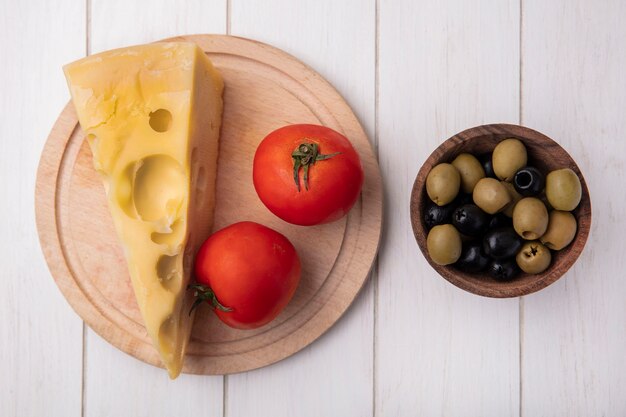 Vista superior do queijo maasdam com tomates em um suporte com azeitonas no fundo branco