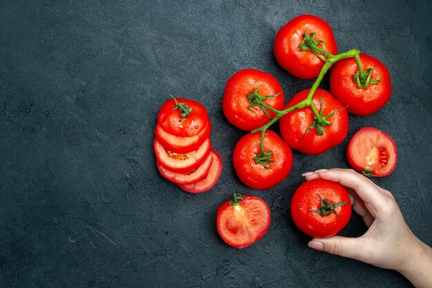 Vista superior do ramo de tomate fresco tomate picado tomate vermelho na mão feminina na mesa preta espaço livre