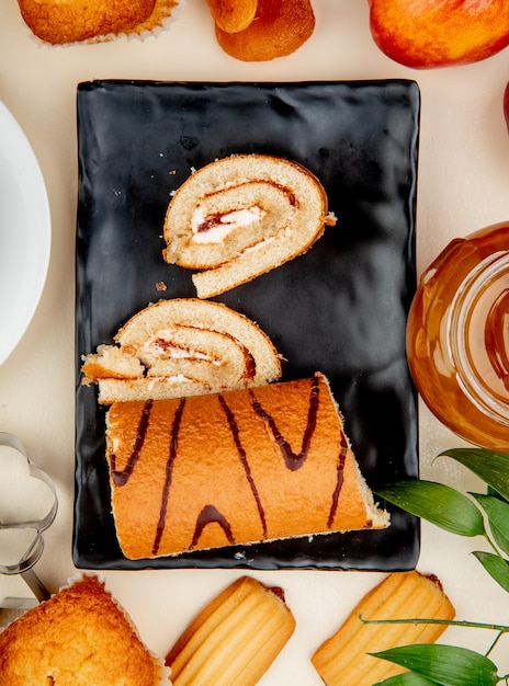 Foto grátis vista superior do rolo cortado e fatiado no prato com biscoitos de bolinho de geléia pêssego ao redor na superfície branca