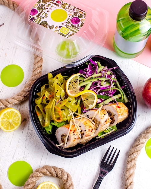 Foto grátis vista superior do rolo de frango recheado com alho vegetal e nozes, servido com salada de repolho e fatia de limão em uma caixa de entrega