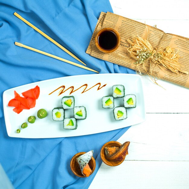 Vista superior do rolo de sushi preto tradicional cozinha japonesa com abacate de arroz e creme de queijo servido com molho de soja, gengibre e wasabi em azul e branco