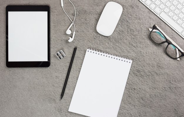 Vista superior do tablet digital em branco; fone de ouvido; rato; teclado e óculos com bloco de notas em espiral